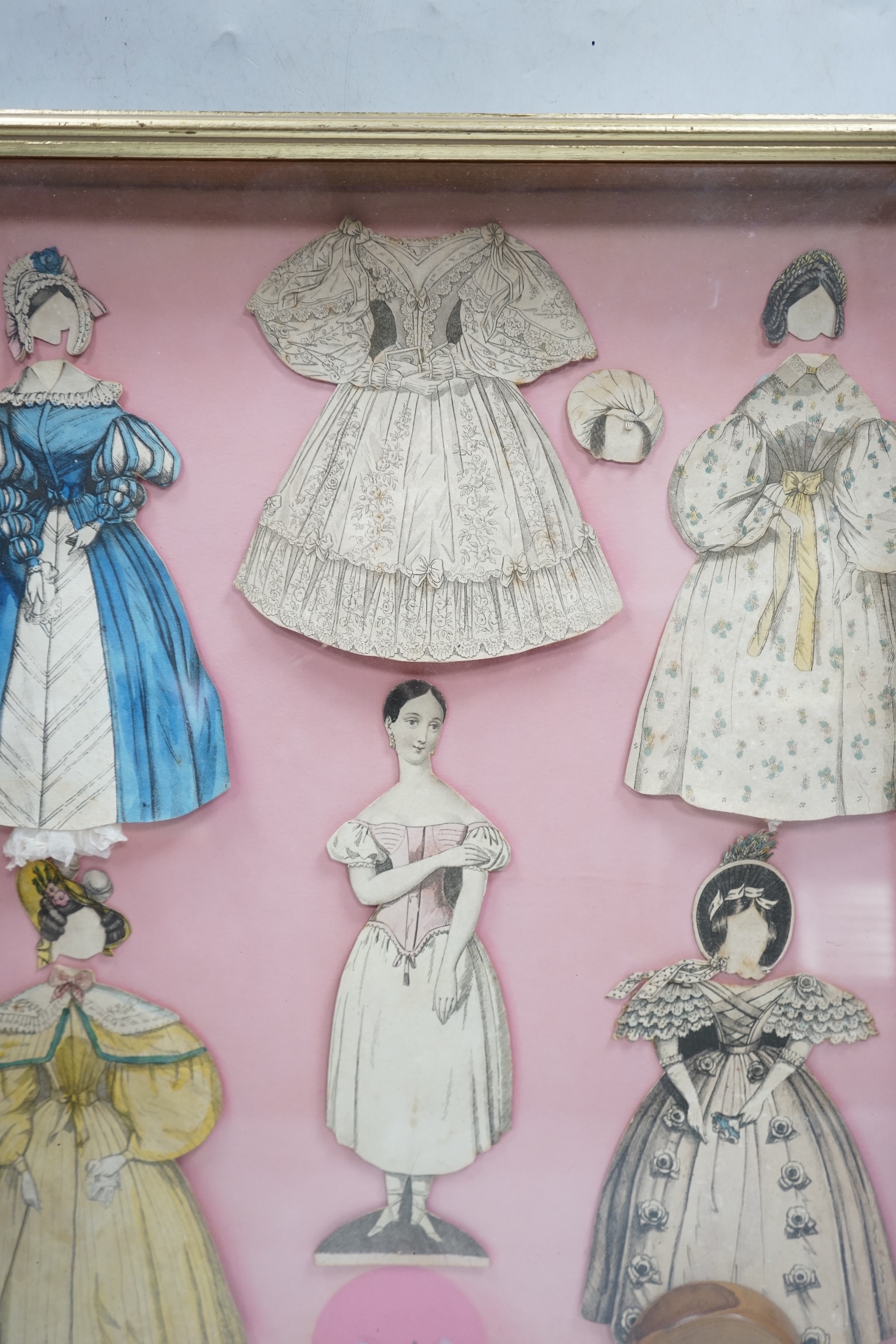 An early 19th century framed Rudolph Ackermann La Poupee-Modele paper doll set, comprising of a double sided doll in lingerie with wooden stand, five double sided gowns and five bonnets, dimensions of the frame; 40cm wid